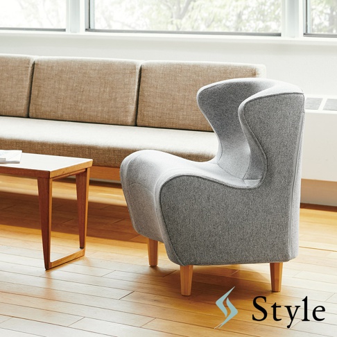 灰色布藝美姿調整座椅，椅背呈流線型，搭配木質椅腳，置於淺色沙發與木桌旁。
