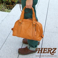 職人手作皮革水洗加工迷你波士頓包，呈淺棕色，由天然皮革製成，包身圓潤，有兩個提把和可拆卸的肩帶，搭配同色系皮革吊牌，整體風格自然樸實。