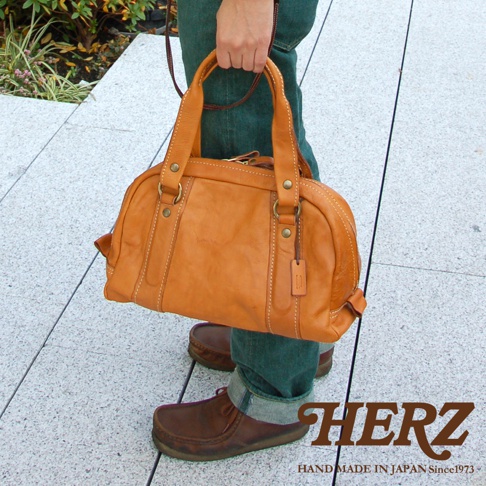 職人手作皮革水洗加工迷你波士頓包，呈淺棕色，由天然皮革製成，包身圓潤，有兩個提把和可拆卸的肩帶，搭配同色系皮革吊牌，整體風格自然樸實。