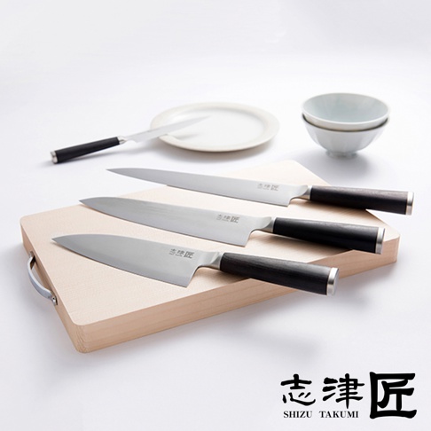 志津匠都系列廚刀，包含一把 Utility knife 多功能刀、兩把主廚刀，以及一把較小的日式廚刀，整齊擺放在木質砧板上，旁邊還有白色餐盤與碗。