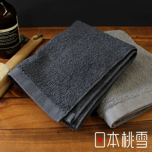 兩條疊放的深灰色和淺灰色毛巾，旁邊放著一瓶深色瓶身的洗浴用品和一個木柄毛刷。