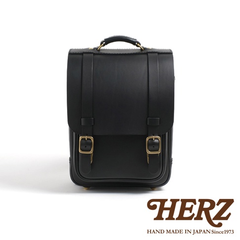 黑色職人手作皮革小學生書包，方正造型，設有兩個金屬釦環及提把。