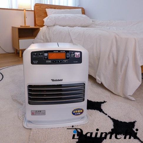 一臺大日Dainichi電子式煤油暖氣機，機身白色，配備橘色螢幕和多個按鈕，擺放在舖有黑白圖案地毯的房間，背景是床鋪和床頭櫃，旁邊還有一個立燈。