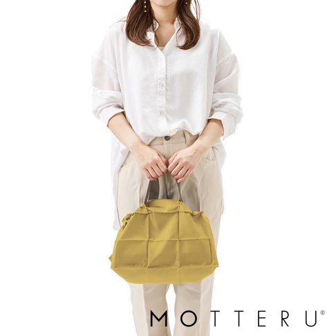 一位女性手提著芥末黃色的輕時尚束口摺疊隨行袋，袋身有菱格紋縫線，束口設計，材質類似尼龍或 polyestery。