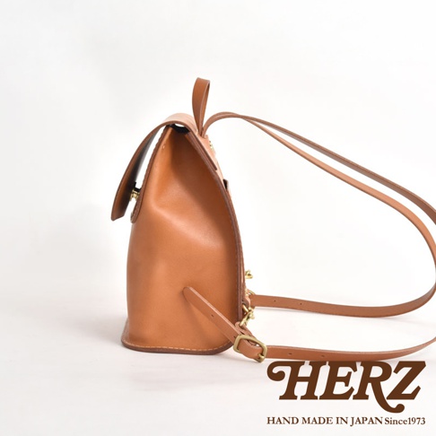 職人手作皮革翻蓋迷你後背包，呈現自然棕色調，以優質皮革製作，設有可調節肩帶和金屬扣件，設計簡約實用。