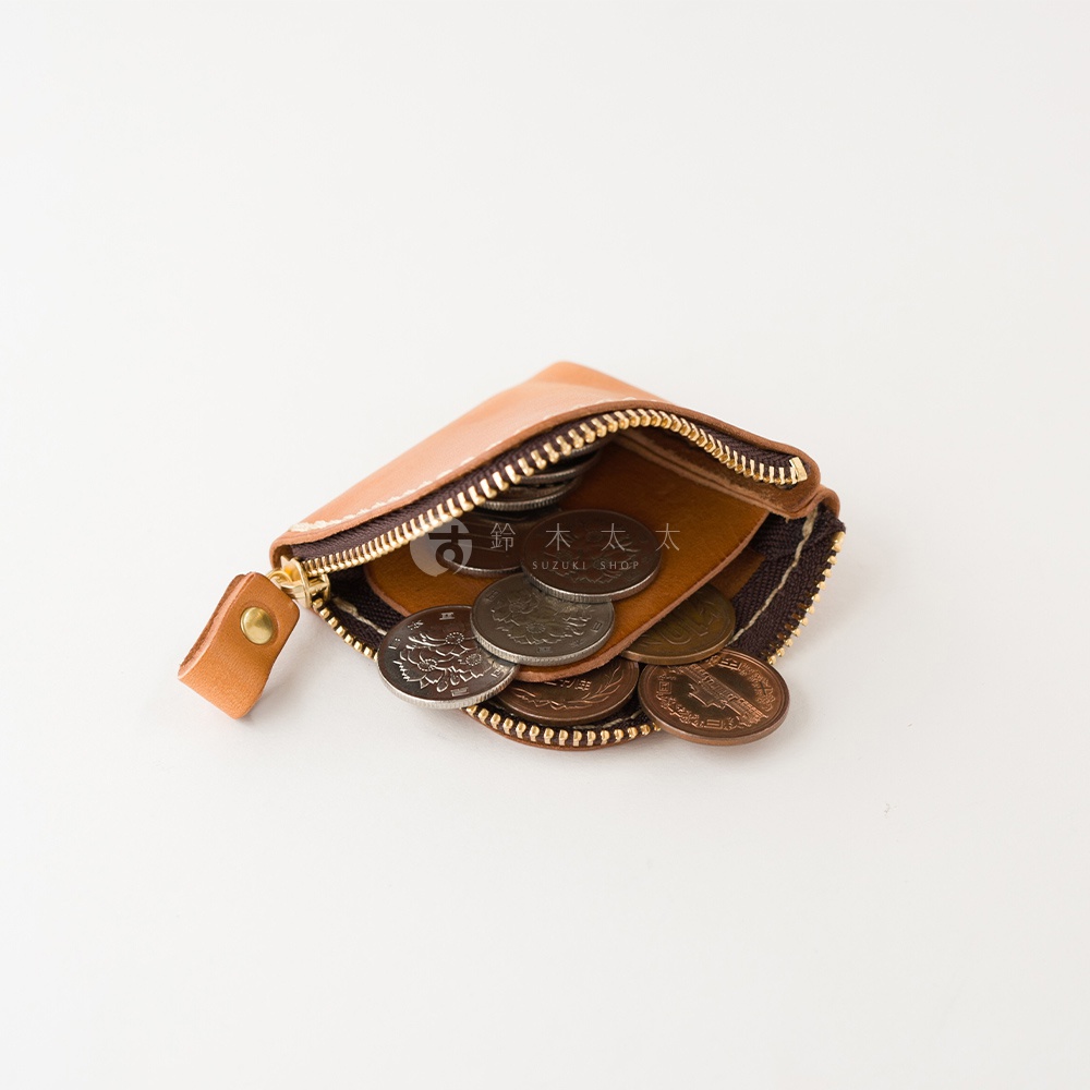 一個採用棕色皮革手工縫製的方形零錢包，拉鍊呈現半開狀態，內部裝滿了多枚日本錢幣，皮革表面隱約可見鈴木太太的標誌，整體設計簡約實用。