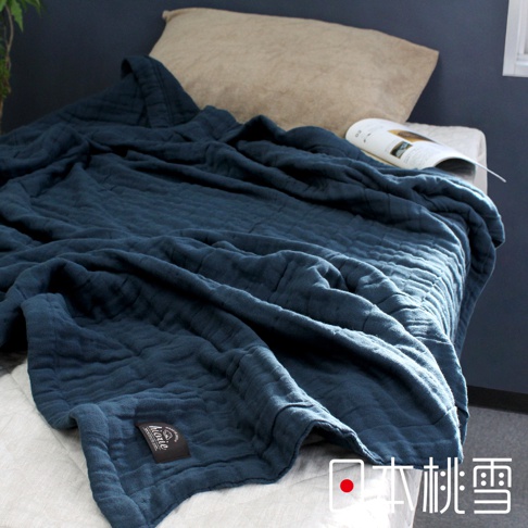 深藍色八層紗透氣被，材質柔軟，表面有菱形格紋，蓋在白色床單上，一旁有米色枕頭和一本打開的雜誌。