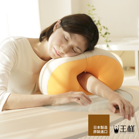 女性臉部靠在橘色與米白色相間的「王樣午睡枕」上，枕頭呈現U型，材質柔軟。