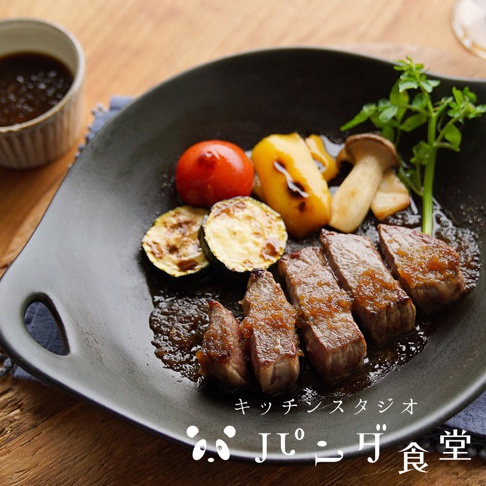 Kitchen Studio Panda食堂的多用途耐熱料理盤盛裝著烤牛排、烤櫛瓜、烤番茄、烤甜椒及香菇，一旁附有醬料碗。