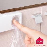 白色的塑膠收納袋架，架上有個圓形開口，手指正將一個透明塑膠袋從開口抽出，架子固定在淺木紋的櫃體上。