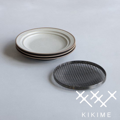 一疊淺色美濃燒餐盤，盤緣帶有深色線條，旁邊放著一個全黑的瀝油網。