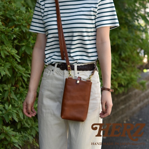 棕色皮革製作的職人手作兩用手機包，附可拆卸斜背帶，包款為長方形設計，配有金屬釦。