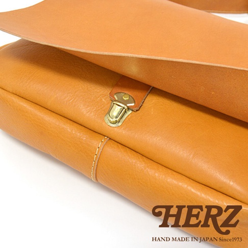 日本HERZ手作皮革軟皮橫式斜背包，特寫其天然皮革材質的細緻紋理與精緻金屬扣細節。