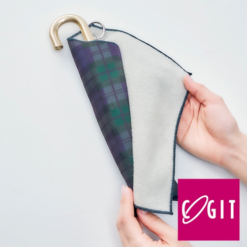 一隻手拿著印有深紫色與綠色格紋的吸水速乾便攜傘套（短款），另一隻手撐開傘套，露出淺灰色內裡。傘套頂端有金色金屬掛鉤與掛環。