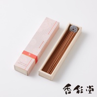 一盒粉色帶有白色螺旋圖案的長方形紙盒，盒蓋旁是裝有許多淺褐色細長線香的淺色木盒，木盒內有一個銀色圓形香座。