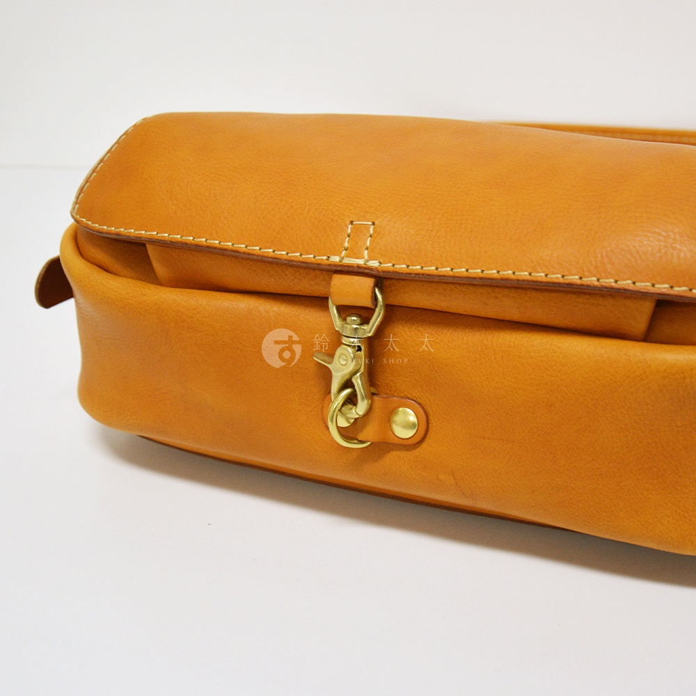 職人手作皮革復古翻蓋郵差包，採用天然皮革製成，呈現溫潤的淺棕色調。包款設有金屬鉤扣與銅釦，搭配細緻的縫線，展現經典復古風格。