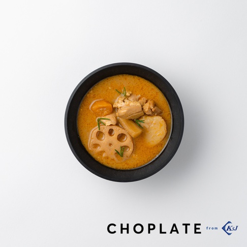 黑色CHOPLATE沙拉碗裝有濃郁的咖哩湯，內含雞肉塊、切片蓮藕、馬鈴薯塊及紅蘿蔔塊，上方裝飾有細綠葉。