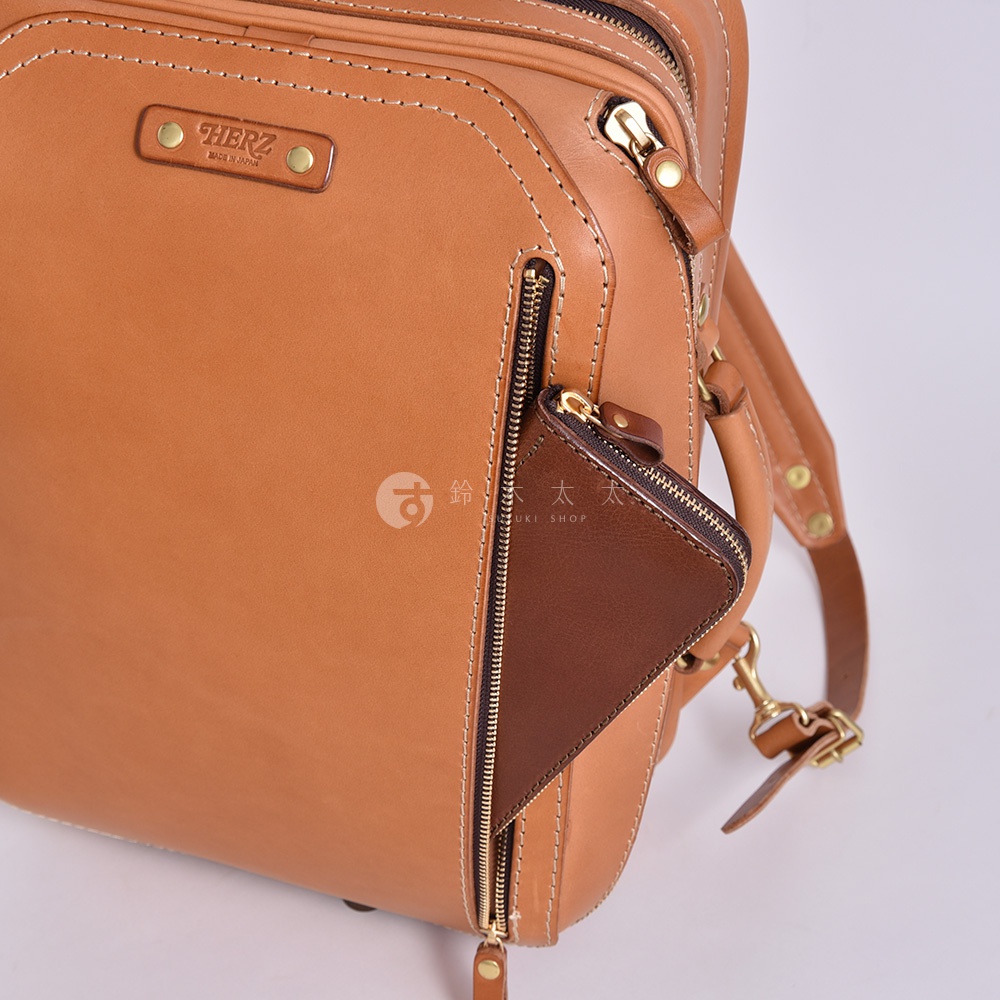 職人手作皮革兩用商務後背包 R-33，展示淺棕色皮革主體，搭配深棕色皮革小零錢包。包包上有精緻的縫線、黃銅色拉鍊和品牌標誌。