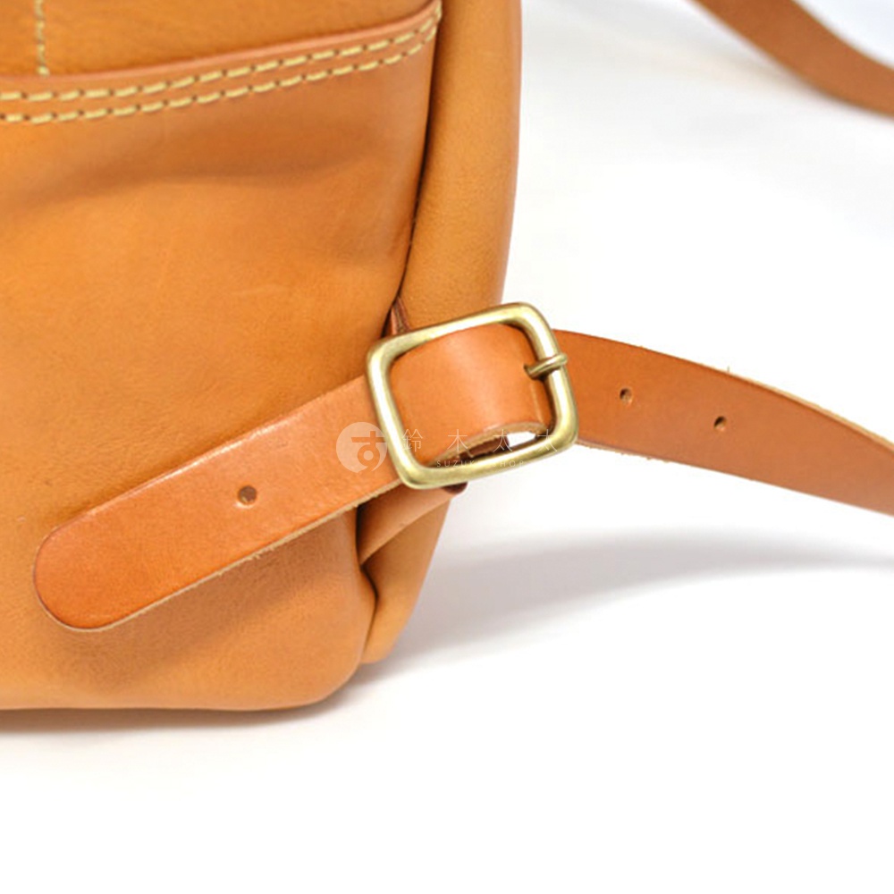 職人手作皮革後背包，棕色皮革材質，側面特寫，展示可調節的皮質揹帶與黃銅色金屬釦環。