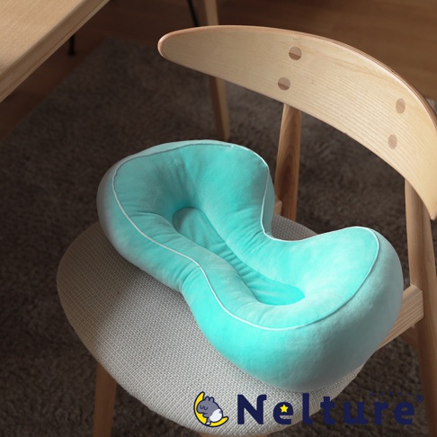 一個土耳其藍色的美姿矯正坐墊，放置在一張木椅的坐墊上，坐墊有獨特的曲線設計，邊緣有白色滾邊，椅子背部為木質彎曲造型。
