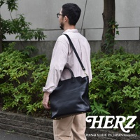 黑色皮革兩用托特包，配有可調節肩帶，包身線條流暢，底部設有金屬腳釘。