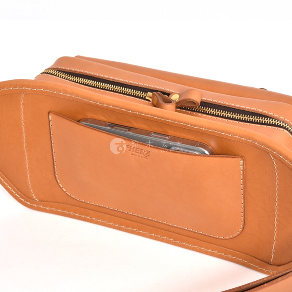 職人手作皮革騎士隨身斜背包，採用淺棕色皮革製成，包體表面縫線清晰，設有拉鍊主袋和一個可放置手機的外置口袋。