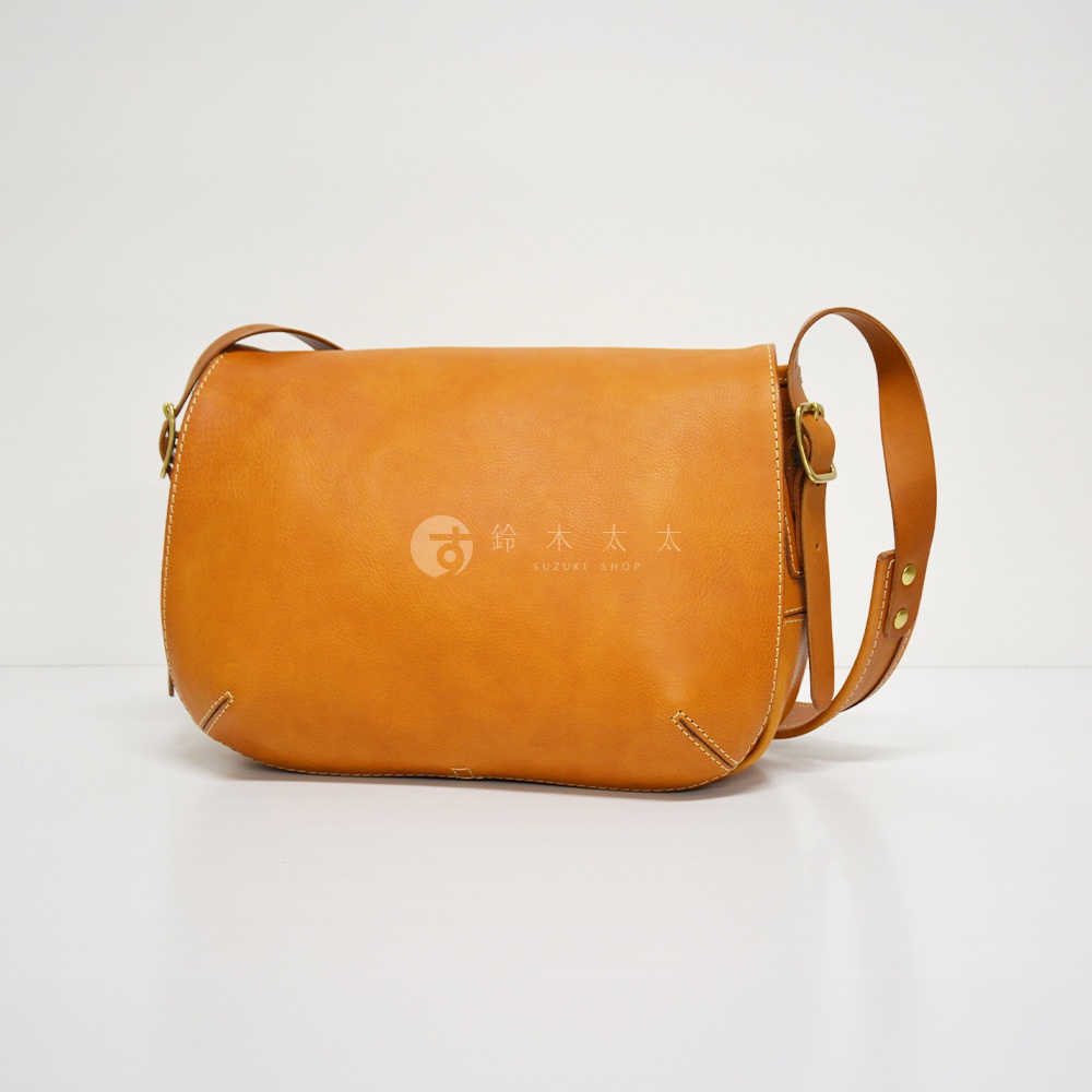 職人手作皮革復古翻蓋郵差包，琥珀色皮革材質，配有可調節的皮革肩帶及金屬扣環。