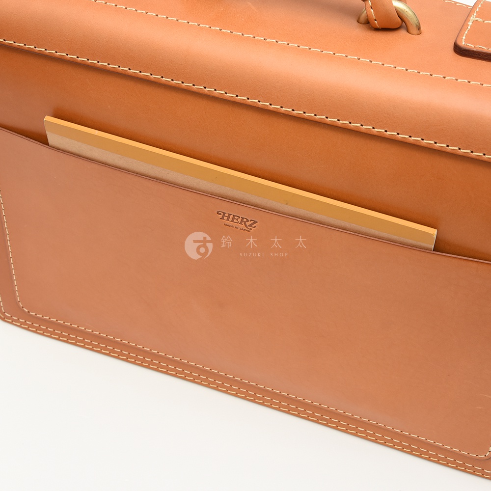 職人手作皮革機師箱，經典棕色皮革，車縫線精緻，箱體一側設有方便置物的內袋，內袋中可見一本黃色封面的筆記本。