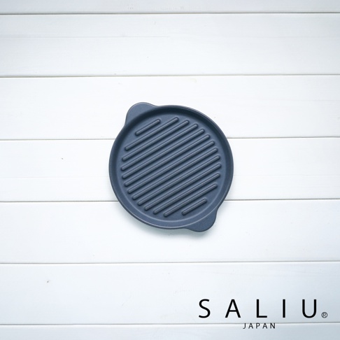 深灰色圓形陶製烤盤，表面有均勻的條狀紋路，兩側有小提把，置於白色木紋背景上。