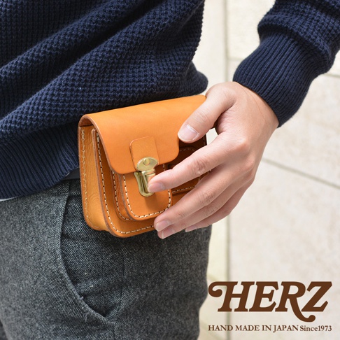 職人手作皮革高爾夫腰包，採用淺棕色皮革製成，配有黃銅鎖扣和米白色縫線，腰包夾在灰色褲子上。