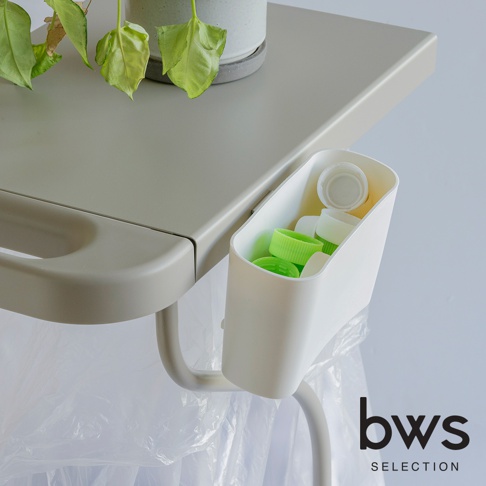 bws SELECTION 簡約滑蓋式分類垃圾架，掛在灰色桌面旁，裡面裝有綠色和白色的瓶蓋，下方有透明垃圾袋。