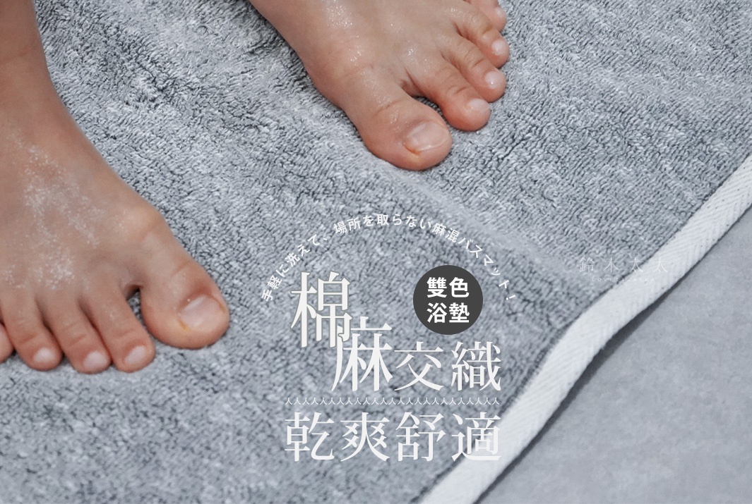 一雙濕潤的腳踩在灰色棉麻混紡浴墊上，浴墊有著細緻的紋理和白色滾邊。