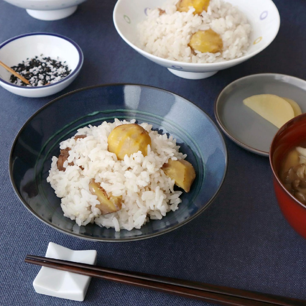 深藍色陶瓷平茶碗盛有栗子飯，碗邊緣帶有綠色線條。