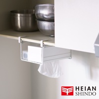 白色金屬材質的免鑽櫥櫃置物架，懸掛於櫥櫃下方，架上放置一盒白色紙巾，下方垂掛著白色垃圾袋。