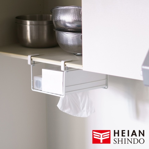 白色金屬材質的免鑽櫥櫃置物架，懸掛於櫥櫃下方，架上放置一盒白色紙巾，下方垂掛著白色垃圾袋。