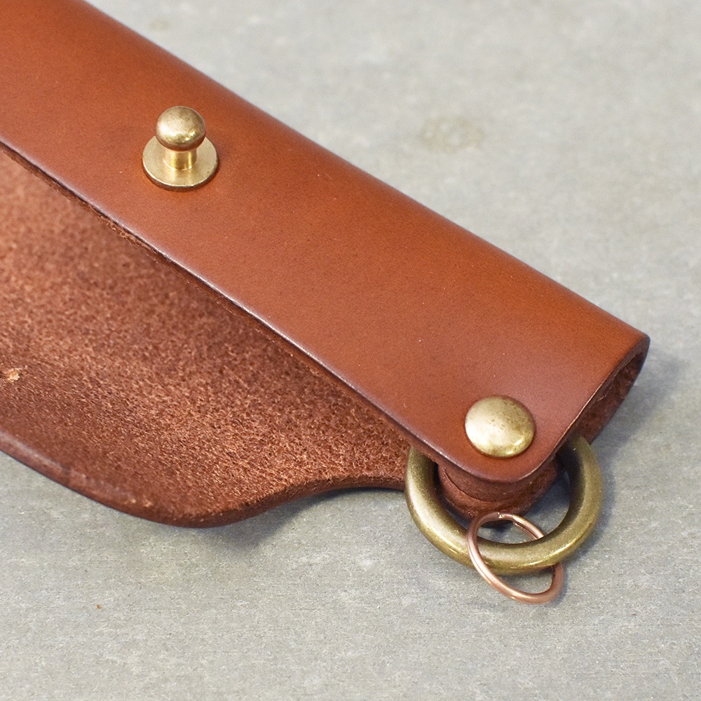 職人手作皮革鑰匙套，採用鞣製皮革製成，表面為光滑的棕色皮革，內裡為麂皮質感。兩側設有黃銅色金屬按扣，底部有一組黃銅色金屬鑰匙圈，可掛鑰匙。
