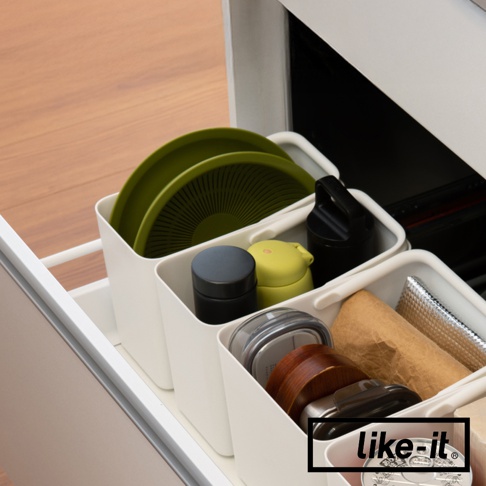 like-it 品牌標誌出現在收納盒內的右下角，收納盒內裝有綠色盤子、黑色和黃綠色容器、木製餐具和金屬罐，用於廚房收納。