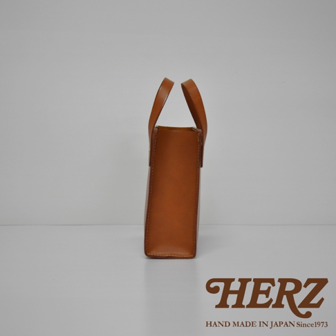 淺棕色皮革直式托特包，簡約設計，兩側有提把，材質為皮革，品牌標誌印在下方。