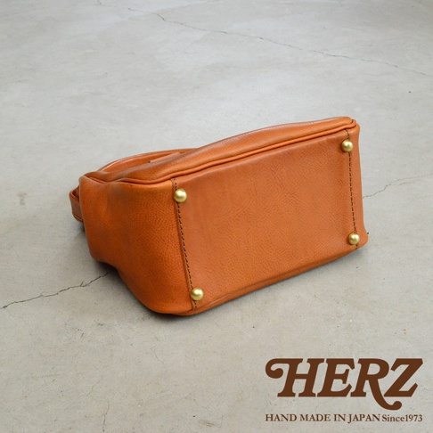 焦糖色職人手作皮革方形口金托特包，底部有四個金色鉚釘，展現皮革質感與精緻縫線。