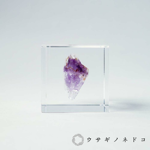 透明立方體內嵌紫水晶礦石，呈現紫色與透明的漸層，礦石表面帶有天然紋理和些許雜質。