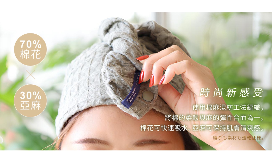 QULM 棉麻混紡吸水速乾包頭巾，採用70%棉花與30%亞麻混紡材質，具備獨特的格紋織法，呈現灰色，頭巾上有品牌標籤，由女性手指調整固定。