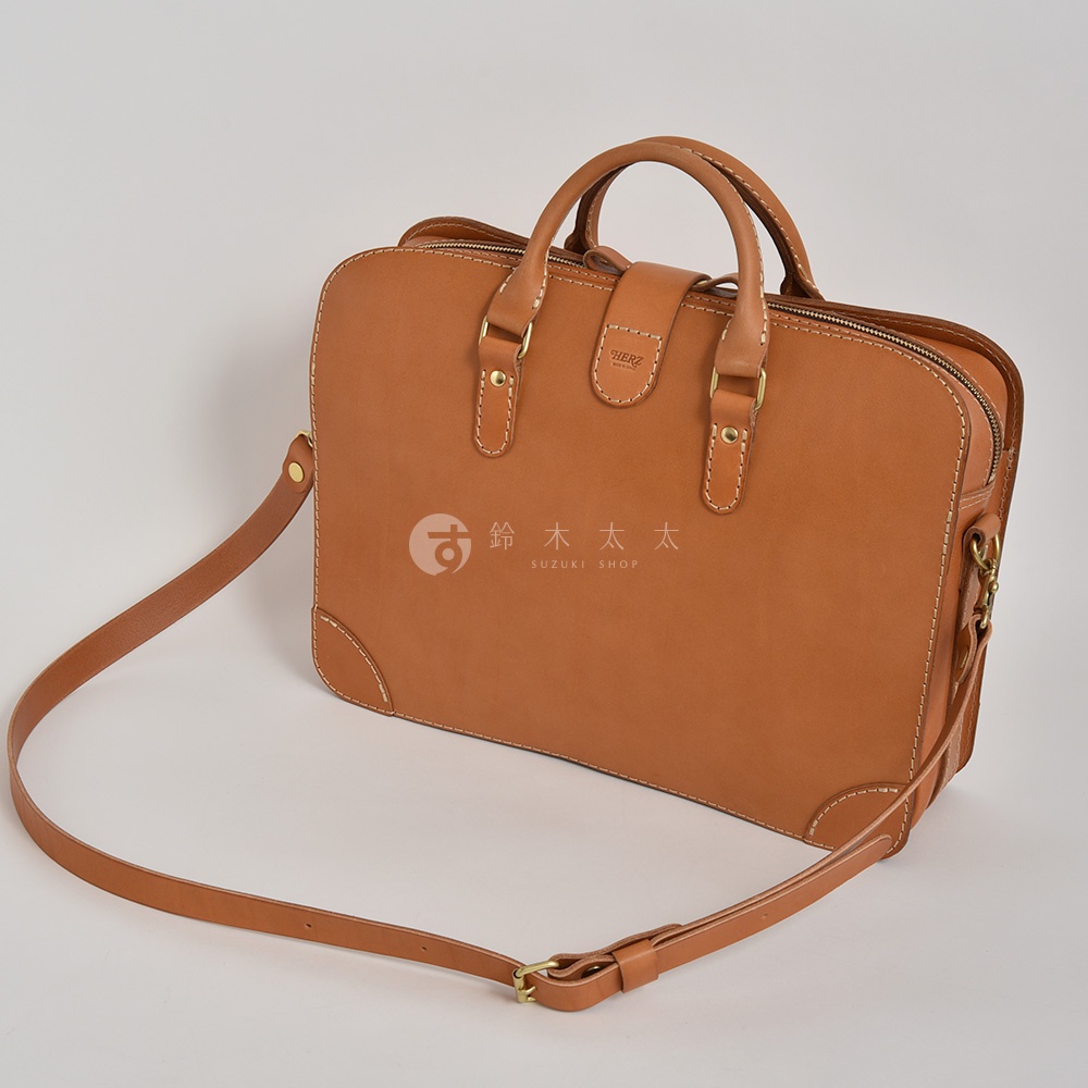 棕褐色皮革製成的手提公事包，有頂部提把、可拆卸肩帶和金屬扣環。包身有縫線細節，正面有品牌標誌。