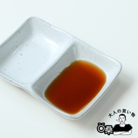 一個淺灰色的陶瓷醬料碟，分為兩個隔間，其中一個隔間盛有深棕色的壽喜燒醬。