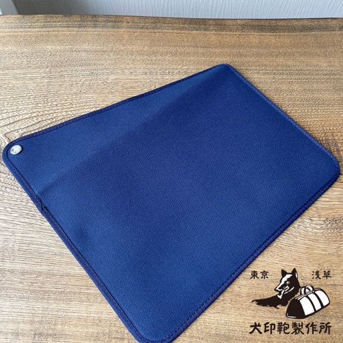 深藍色純綿帆布平板收納包，材質耐磨，邊緣車縫線整齊，左上角有金屬鈕扣。