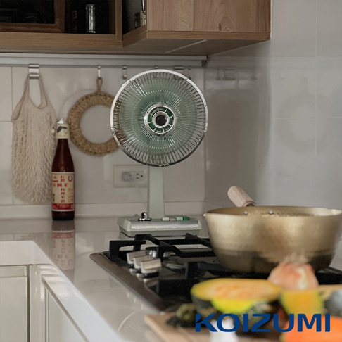 復古風格的白色電風扇，扇葉為綠色，金屬網罩，置於廚房檯面上。
