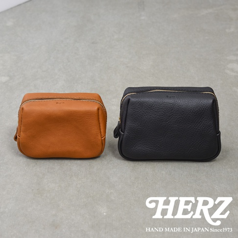 兩個日本HERZ職人手作皮革Organ拉鍊收納包並排擺放，左側為焦糖色，右側為黑色，兩者皆為長方形圓角設計，表面印有小巧的Organ品牌標識，下方印有HERZ的品牌名稱與手作標語。