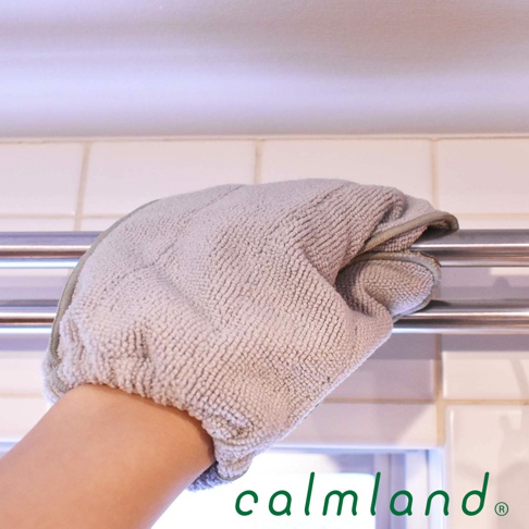 一隻手戴著淺灰色超細纖維除塵清潔手套，正在擦拭金屬桿。手套材質柔軟，表面有細密的絨毛。