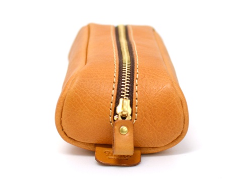一個棕褐色皮革製、圓角設計的收納筆袋，配有黃銅拉鍊和深棕色縫線。筆袋底部有一個皮革標籤，上面印有品牌資訊。