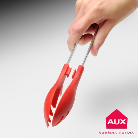 手持一對紅色不沾桌快手料理夾，料理夾由不鏽鋼夾臂和紅色矽膠夾頭組成，夾頭設計有方便夾取的凹槽。