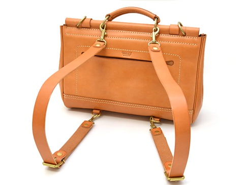 職人手作皮革屋瓦風三用側背包，採用天然鞣製皮革，呈現溫潤的淺棕色。包款設計簡約，配有可拆卸式肩背帶和後背帶，以及頂部提把，可肩背、後背或手提。包身上有精緻縫線和金屬扣環，風格經典。